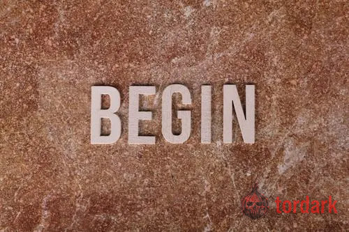 The word 'BEGIN' in pale block letters laid on a warm, reddish-brown stone surface