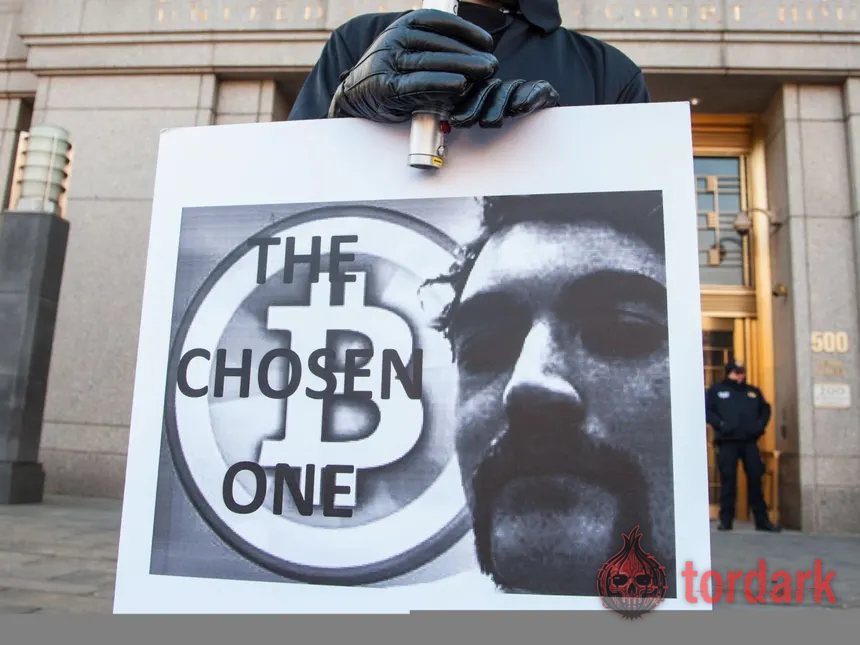 A supporter outside the Manhattan federal courthouse holding a sign reading 'THE CHOSEN ONE' over a Bitcoin symbol and an image of Ross Ulbricht